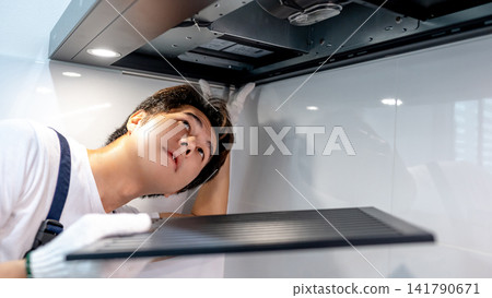 Asian male technician removing range metal filter looking inside the cooker hood Asian male technician removing range metal filter looking inside the cooker hood 141790671