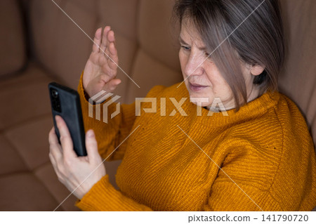 Mature woman having video call on smartphone, waving hand 141790720