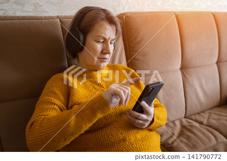 Mature woman listening to music browsing smartphone at home Mature woman listening to music browsing smartphone at home 141790772