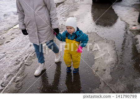 Parent and child walking outdoors on melting snow Parent and child walking outdoors on melting snow 141790799