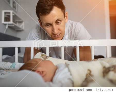 Father watching over his sleeping baby in crib 141790804