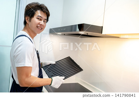 Asian male maintenance worker looking at camera while holding black range hood filter Asian male maintenance worker looking at camera while holding black range hood filter 141790841