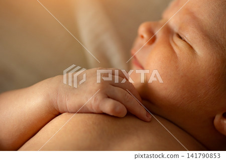 Newborn baby hand resting on parent shoulder sleeping Newborn baby hand resting on parent shoulder sleeping 141790853