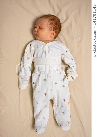 Newborn child wearing pajamas on light blanket Newborn child wearing pajamas on light blanket 141791149