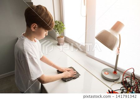 Young boy cleaning white desk with cloth at home Young boy cleaning white desk with cloth at home 141791342