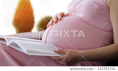 Pregnant woman reading book and touching belly with caring hand Pregnant woman reading book and touching belly with caring hand 141791358