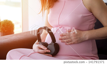 Pregnant woman holding headphones on her belly Pregnant woman holding headphones on her belly 141791371