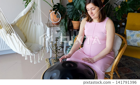 Pregnant woman playing handpan for relaxation and wellness Pregnant woman playing handpan for relaxation and wellness 141791396