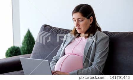 Pregnant woman working from home on laptop Pregnant woman working from home on laptop 141791443