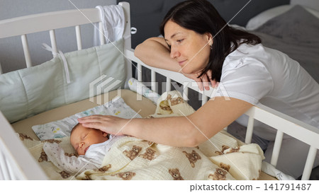 Mother gently caressing sleeping newborn baby in crib Mother gently caressing sleeping newborn baby in crib 141791487