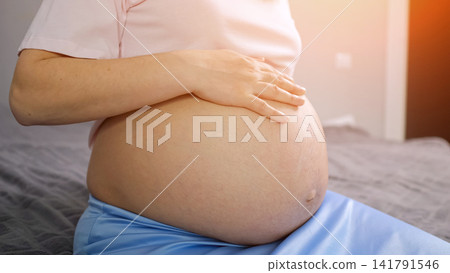 Pregnant woman gently touching her baby bump at home Pregnant woman gently touching her baby bump at home 141791546