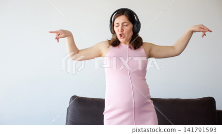 Pregnant woman enjoying music and dancing with headphones Pregnant woman enjoying music and dancing with headphones 141791593