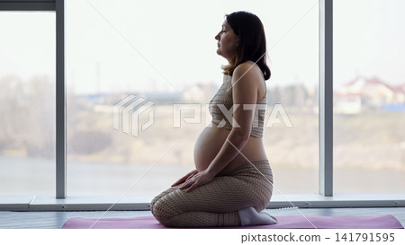 Pregnant woman meditating while practicing yoga indoors Pregnant woman meditating while practicing yoga indoors 141791595