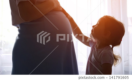 Daughter touching pregnant mother's belly, anticipating new sibling Daughter touching pregnant mother's belly, anticipating new sibling 141791605