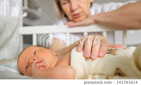 Grandmother comforting newborn baby resting in crib Grandmother comforting newborn baby resting in crib 141791614
