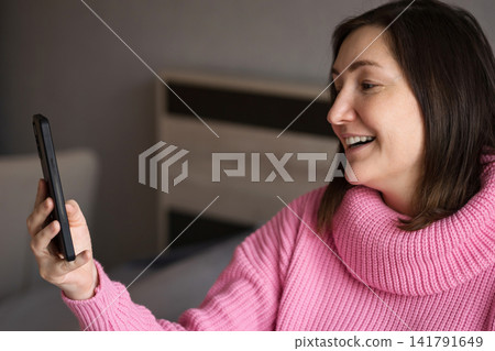 Pregnant woman smiling while holding a smartphone indoors Pregnant woman smiling while holding a smartphone indoors 141791649