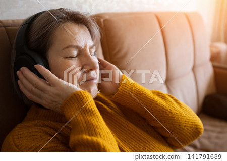 Relaxed woman wearing headphones resting on a sofa in warm home interior light Relaxed woman wearing headphones resting on a sofa in warm home interior light 141791689