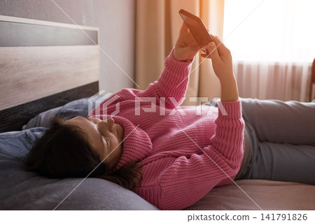 Pregnant woman in cozy knit dress stretching on bed at home with warm morning sunlight Pregnant woman in cozy knit dress stretching on bed at home with warm morning sunlight 141791826