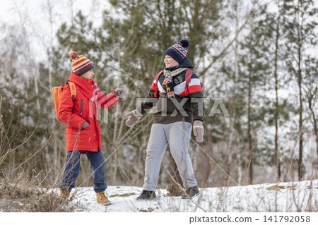 Two children dressed in winter clothing talking on a snowy hill with trees in the background Two children dressed in winter clothing talking on a snowy hill with trees in the background 141792058