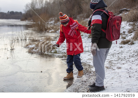 Two boys with school backpacks walk on thin dangerous ice on a frozen river Two boys with school backpacks walk on thin dangerous ice on a frozen river 141792059