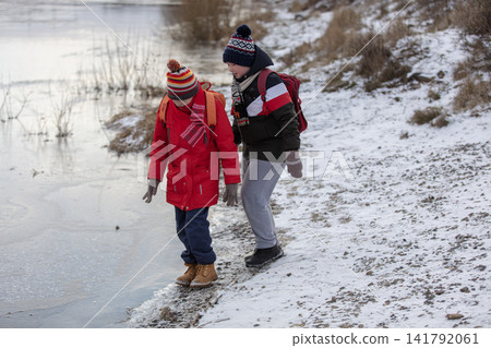 Two children stand by a frozen river and look at the water. Two children stand by a frozen river and look at the water. 141792061