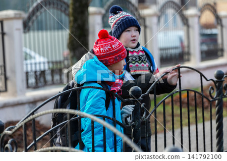 Kids talk by the fence in a neighborhood during winter near their home in the afternoon light Kids talk by the fence in a neighborhood during winter near their home in the afternoon light 141792100