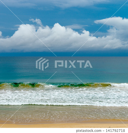Tropical coastline scenery featuring golden sand and blue sea water with foam under cloudy sky Tropical coastline scenery featuring golden sand and blue sea water with foam under cloudy sky 141792718