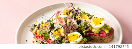 Fresh sandwiches made with gluten free bread topped with beetroot hummus, pesto, boiled quail eggs, and microgreens served on a simple plate, banner Fresh sandwiches made with gluten free bread topped with beetroot hummus, pesto, boiled quail eggs, and microgreens served on a simple plate, banner 141792745