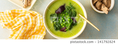 A bowl of creamy broccoli and green pea soup sits on a green plate. Next to it is liver pate in a small dish and grissini on a white platter. This meal provides healthy options, banner A bowl of creamy broccoli and green pea soup sits on a green plate. Next to it is liver pate in a small dish and grissini on a white platter. This meal provides healthy options, banner 141792824
