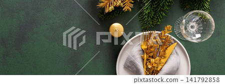 Top view of a Christmas table, featuring an empty plate with a napkin and cutlery on a green surface. Spruse branches and golden tree decorations set a joyful holiday atmosphere, banner Top view of a Christmas table, featuring an empty plate with a napkin and cutlery on a green surface. Spruse branches and golden tree decorations set a joyful holiday atmosphere, banner 141792858