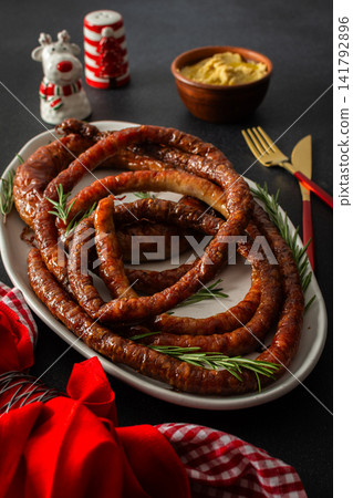 A Christmas table is set with fried pork sausage in the center. Red flowers and festive decorations surround the food as families gather to celebrate during the evening A Christmas table is set with fried pork sausage in the center. Red flowers and festive decorations surround the food as families gather to celebrate during the evening 141792896