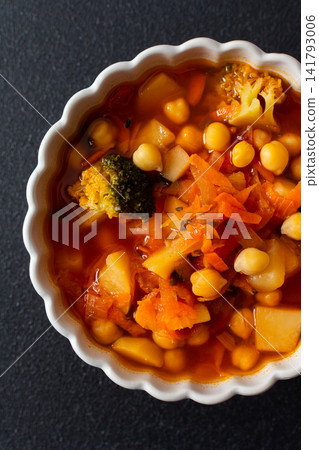 A bowl holds bright red soup made with vegetables like tomatoes, carrots, potatoes, and broccoli, served alongside gluten-free flaxseed bread for a healthy meal A bowl holds bright red soup made with vegetables like tomatoes, carrots, potatoes, and broccoli, served alongside gluten-free flaxseed bread for a healthy meal 141793006