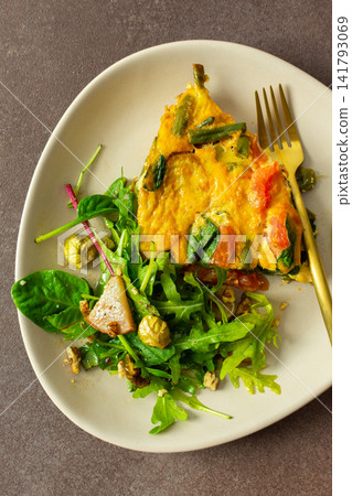 A plate holds baked vegetables combined with eggs alongside a salad of arugula and Brussels sprouts. This meal is perfect for breakfast or lunch, providing healthy nutrients A plate holds baked vegetables combined with eggs alongside a salad of arugula and Brussels sprouts. This meal is perfect for breakfast or lunch, providing healthy nutrients 141793069