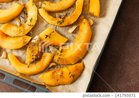 Butternut squash slices are arranged on a tray with herbs and garlic, ready for roasting. This is part of a cooking process in a kitchen setting Butternut squash slices are arranged on a tray with herbs and garlic, ready for roasting. This is part of a cooking process in a kitchen setting 141793071