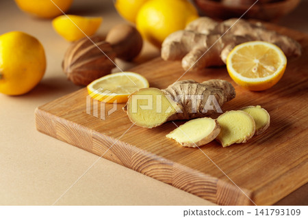 Ginger roots and fresh lemons on a cutting board. Ginger roots and fresh lemons on a cutting board. 141793109