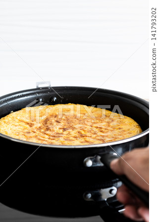 Hand holding frying pan with Spanish potato omelette Hand holding frying pan with Spanish potato omelette 141793202