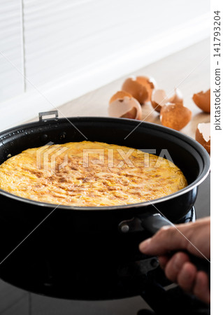 Hand holding frying pan with Spanish potato omelette Hand holding frying pan with Spanish potato omelette 141793204