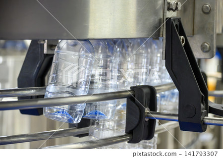 Empty PET bottles moving on overhead conveyor belt in drinking water factory Empty PET bottles moving on overhead conveyor belt in drinking water factory 141793307