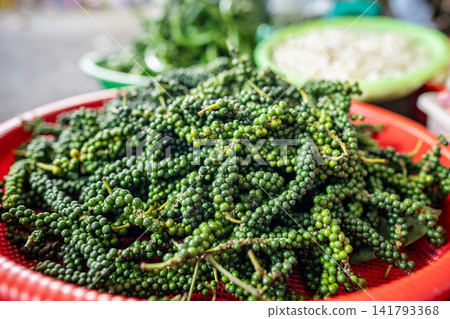 Plastic basket filled with pile of fresh green peppercorns on stem, unripe Piper nigrum vine berries Plastic basket filled with pile of fresh green peppercorns on stem, unripe Piper nigrum vine berries 141793368