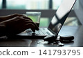 Close-Up of Hands Typing on a Laptop While Enjoying a Drink with Keys Nearby, Illustrating Modern Workspace and Productivity in Daily Life. 141793795
