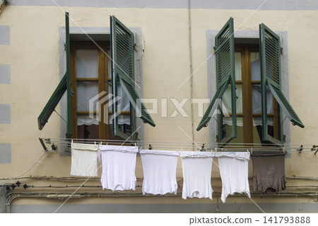 Two wooden windows with green shutters and laundry drying on clothesline Two wooden windows with green shutters and laundry drying on clothesline 141793888