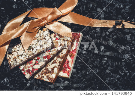 Handmade artisan chocolate bars with nuts and dried fruits decorated with golden ribbon Handmade artisan chocolate bars with nuts and dried fruits decorated with golden ribbon 141793940
