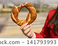Close-up of traditional Turkish simit covered with sesame in hand of an unrecognizable woman seeds outdoors. Popular street food in Turkey, fresh baked circular bread captured in natural sunlight 141793993
