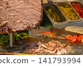 Close-up of traditional Turkish doner kebab meat being sliced and served on hot grill with fresh vegetables and flatbread in background. Authentic Turkish street food  141793994