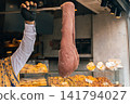 Vendor in traditional embroidered vest stretches large thick mass of chocolate Maras dondurma ice cream on metal rod in shop 141794027