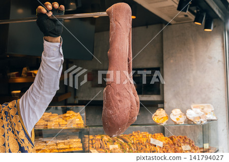 Vendor in traditional embroidered vest stretches large thick mass of chocolate Maras dondurma ice cream on metal rod in shop Vendor in traditional embroidered vest stretches large thick mass of chocolate Maras dondurma ice cream on metal rod in shop 141794027