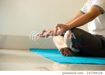 Man practicing yoga meditation in lotus pose on a blue mat with mudra, showing mindfulness, wellness, balance, relaxation, breathing, focus, calm, fitness, and indoor tranquility Man practicing yoga meditation in lotus pose on a blue mat with mudra, showing mindfulness, wellness, balance, relaxation, breathing, focus, calm, fitness, and indoor tranquility 141794126