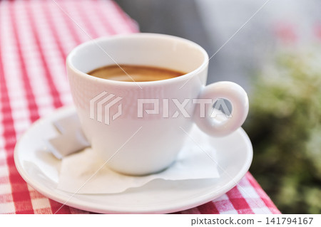 Close-up of a fresh white ceramic cup of hot espresso on checkered tablecloth Close-up of a fresh white ceramic cup of hot espresso on checkered tablecloth 141794167