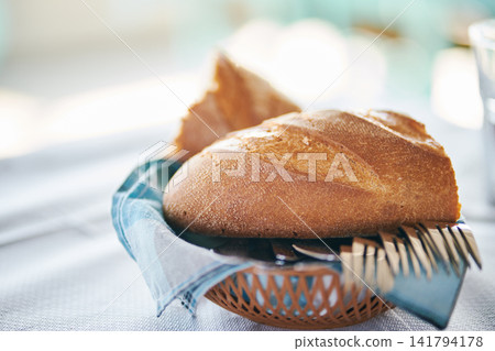 Fresh crusty bread loaf served in a small basket with cutlery on dining table Fresh crusty bread loaf served in a small basket with cutlery on dining table 141794178