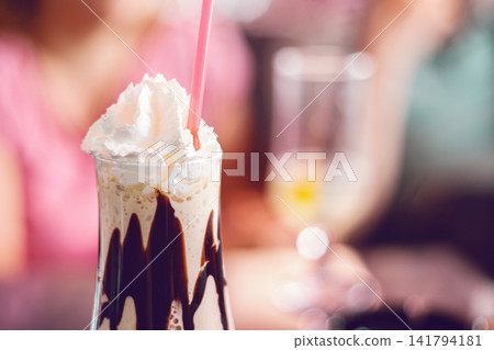 Close-up of a delicious chocolate milkshake topped with whipped cream and a pink straw Close-up of a delicious chocolate milkshake topped with whipped cream and a pink straw 141794181